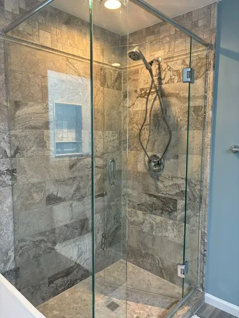 Corner shower with frameless glass, tumbled stone-look tile and a built-in shelf