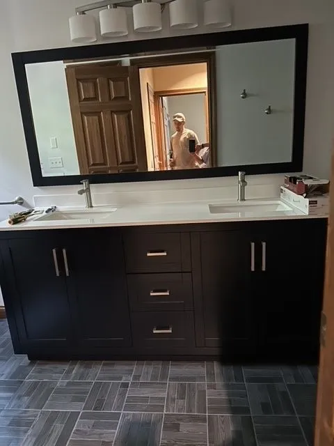 Double vanity installation with espresso cabinets, a quartz top and a black framed mirror