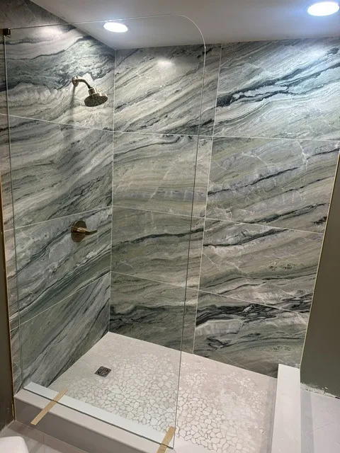 Walk-in shower lined in dramatic green and grey veined marble-look slab tile with brass fixtures