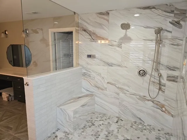 Large walk-in shower in marbled porcelain with a built-in bench and a glass partition