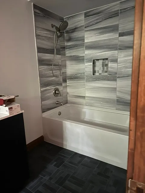 Alcove tub with a dramatic grey marbled tile surround and a mosaic niche