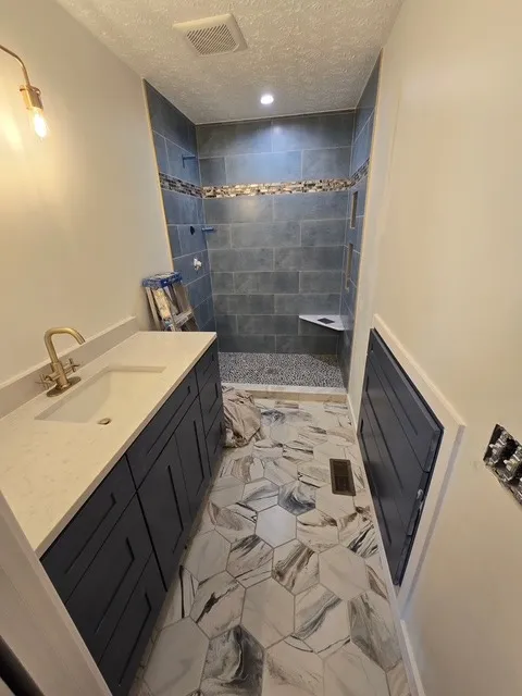 Bathroom remodel with a navy slate tile shower, gold faucet and large hexagon marble-look floor tile