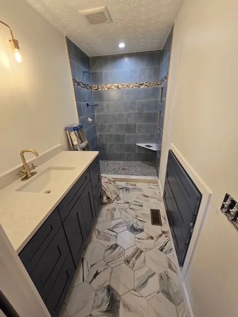 Navy vanity with a brass tap and a stone top, beside a blue tiled shower