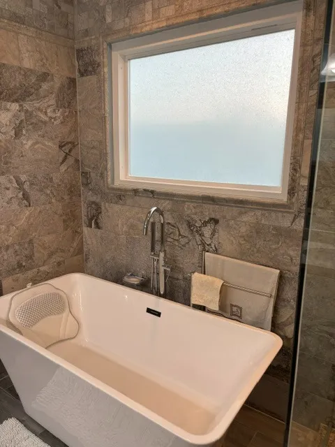 Rectangular freestanding tub with a floor-mounted filler against travertine-look wall tile