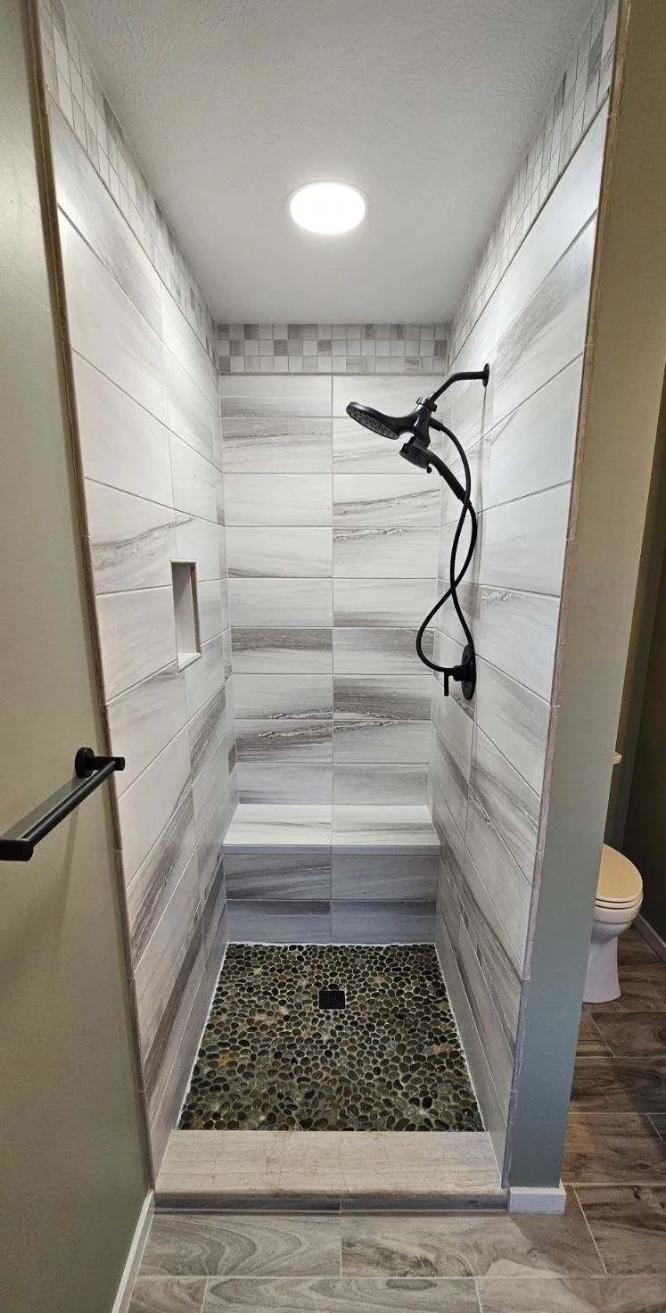 Custom tile walk-in shower with a built-in bench, river rock floor and matte black fixtures