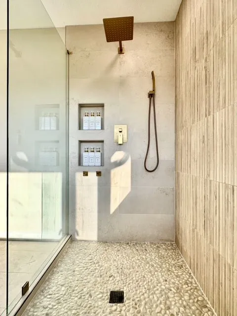 Walk-in shower with a brass rain head, two recessed niches and a pebble tile floor