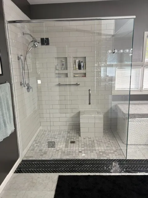 White subway tile shower with a marble mosaic floor and a black chevron tile border
