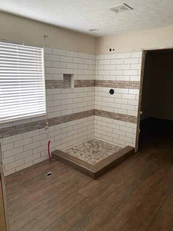 Shower pan and white subway tile walls part-way through a bathroom remodel