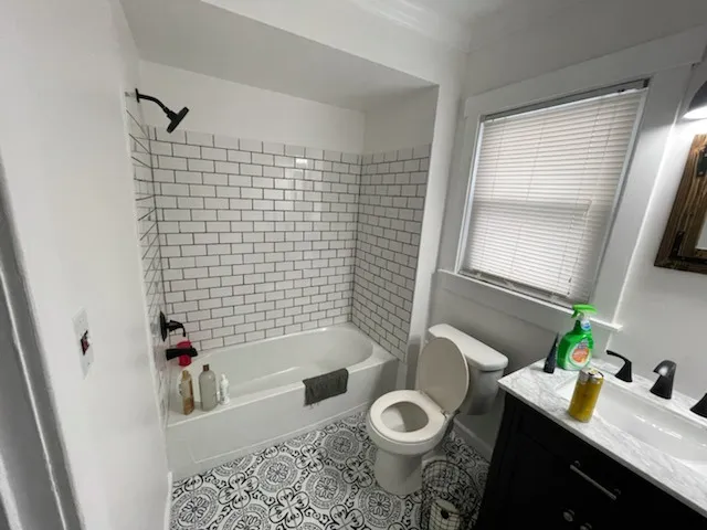 Bathroom with a white subway tile tub surround, black fixtures and patterned floor tile