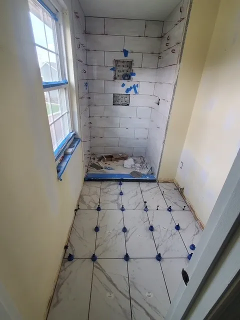 Marble-look floor tile being set with levelling clips during a bathroom remodel