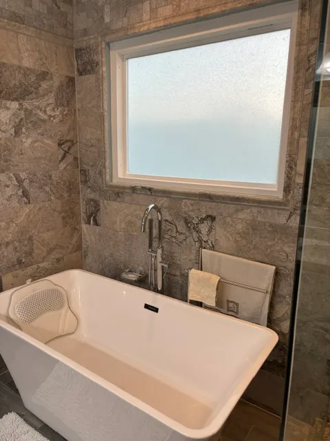 Tub set into a marble-tiled surround under a window