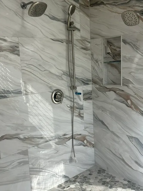 Heavily veined marble shower walls with twin rain heads and a hexagon mosaic floor