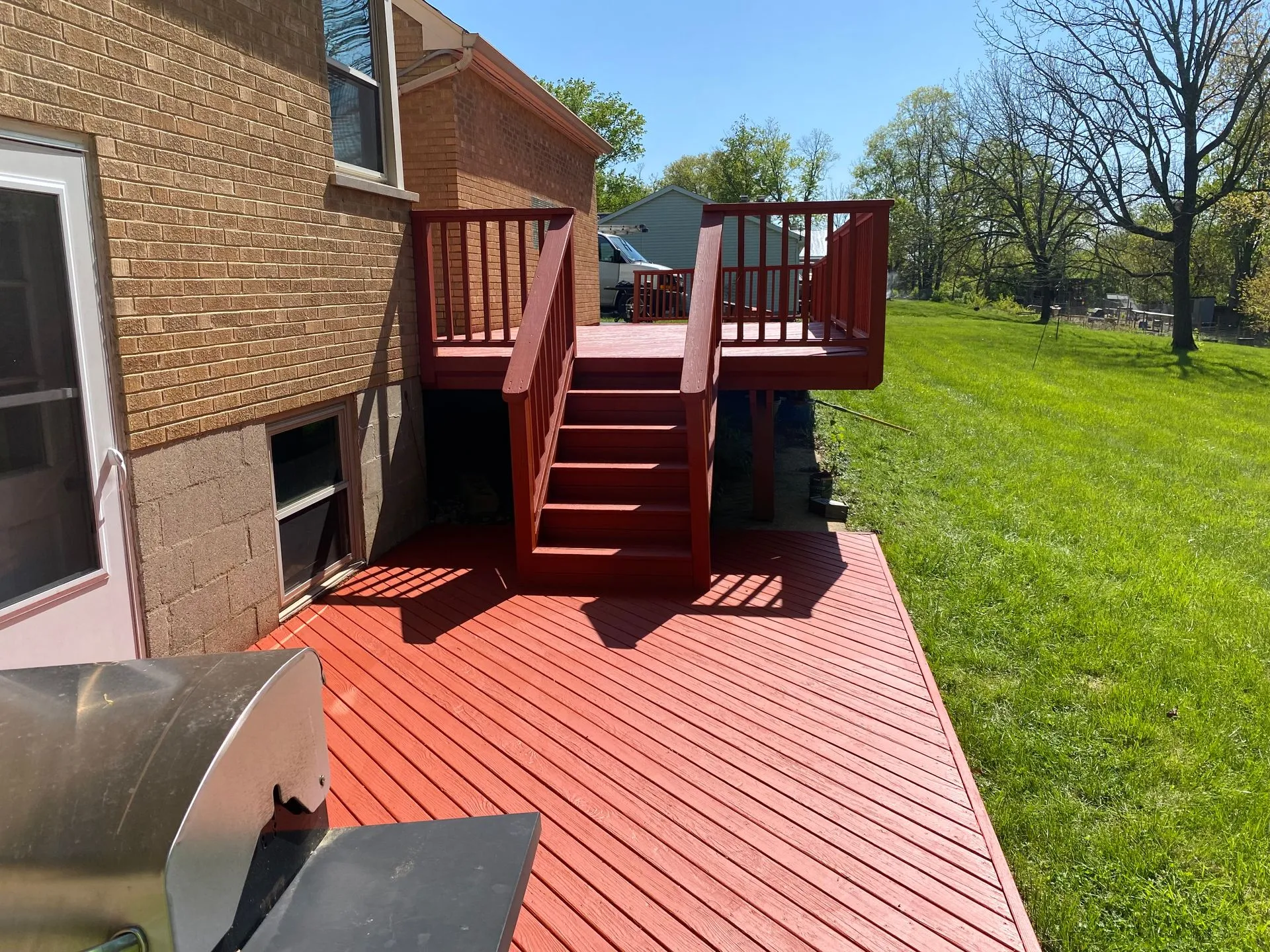 Two-tier backyard deck with stairs and railings finished in a red stain