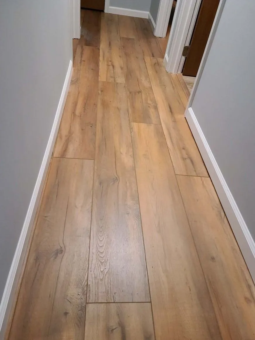 New wide plank oak flooring installed in a hallway with white baseboards