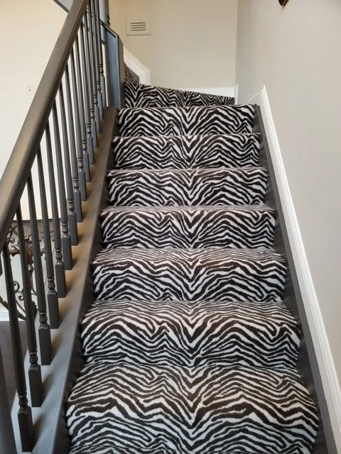 Staircase with a zebra print carpet runner and black iron balusters