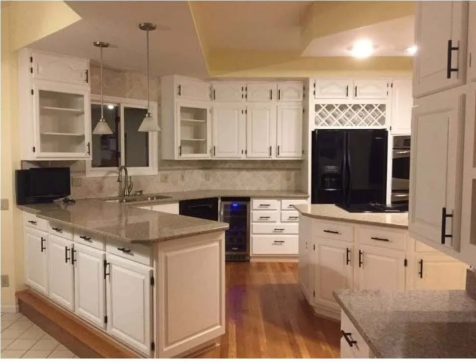 Refinished kitchen cabinets painted white with granite counters and black hardware