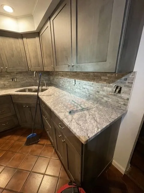 Kitchen remodel in progress with grey stained cabinets, granite counters and a stone tile backsplash