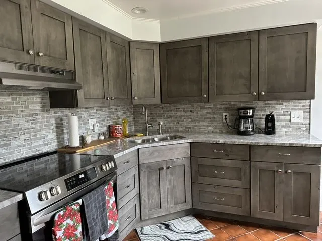 Remodeled kitchen with grey stained shaker cabinets, a stone mosaic backsplash and marble-look counters