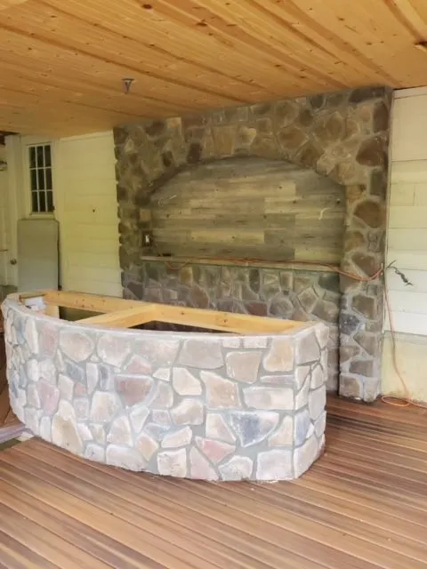 Outdoor living construction — a stone fireplace and curved stone bar under a covered deck