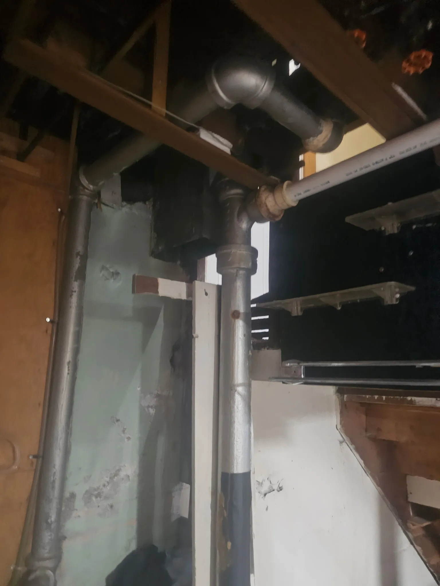 Cast-iron drain stack and new supply lines roughed in inside an opened wall cavity, framing exposed
