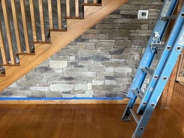 Stone accent wall being installed under a wooden staircase